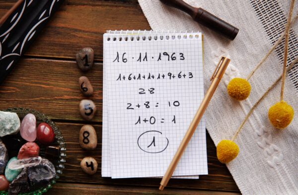 Cahier de numérologie posé sur une table en bois, entouré de pierres énergétiques, avec un calcul de chemin de vie menant au chiffre 1, symbolisant l'analyse spirituelle.