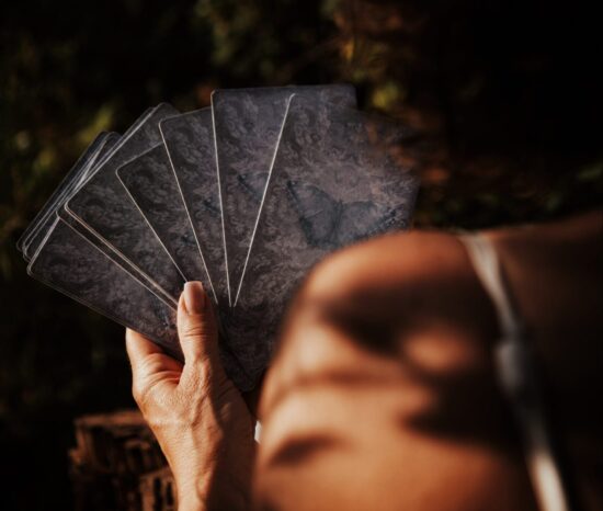 Main tenant un éventail de cartes divinatoires éclairées par une lumière douce et naturelle.